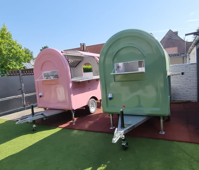 Zwei farbige Imbisswagen, rosa und grün, stehen auf einer gepolsterten Fläche.