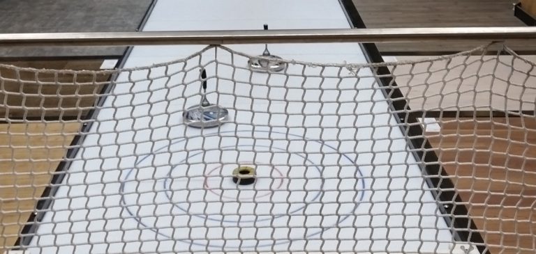 Curlingbahn mit einem Spielstein im Zielbereich und einem Netz im Hintergrund.