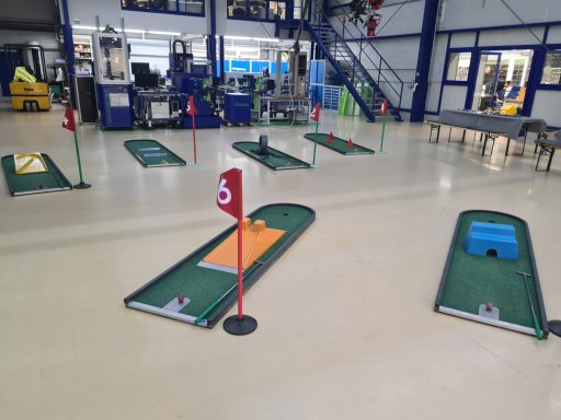 Minigolfanlage mit mehreren Bahnen und Schildern in einer großen Halle.