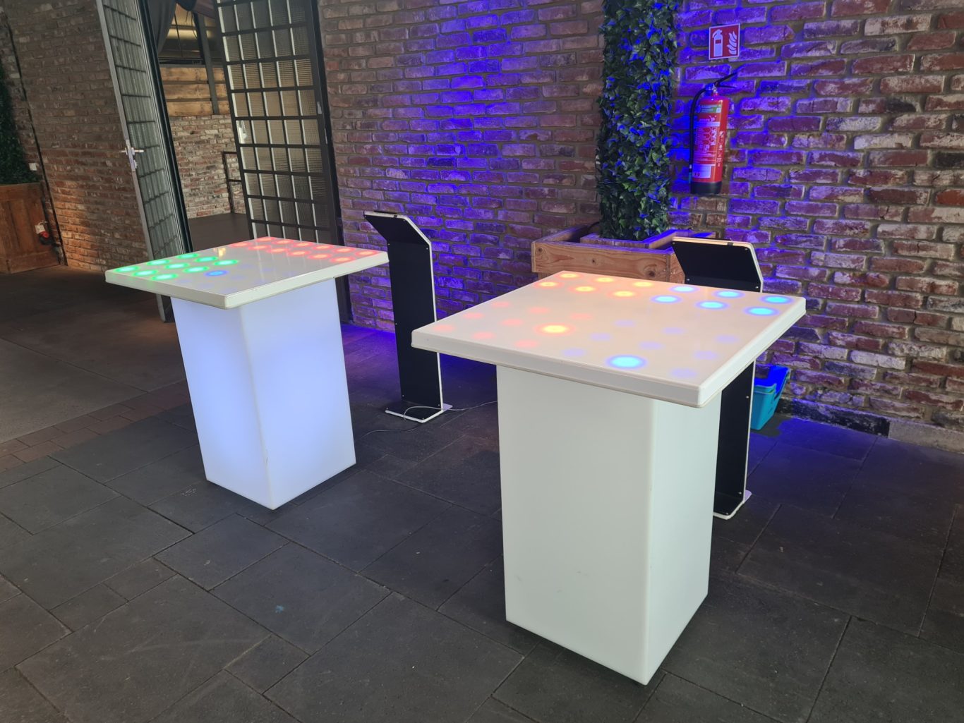 Reaktionstisch - Reaction Desk Zwei helle Stehtische mit bunten Lichtern in einer modernen Umgebung.