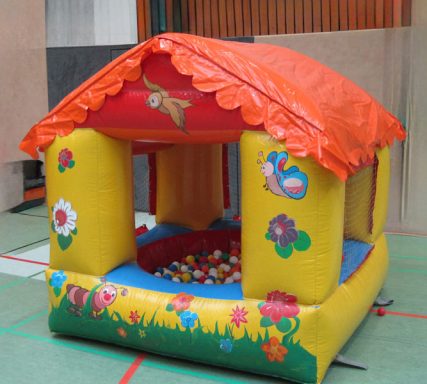 Buntes Hüpfhaus mit einem roten Dach und einem Sofa voller bunter Bälle.