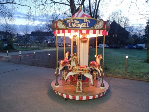 Karussell mit bunten Pferden, beleuchtet bei dusk, umgeben von Bäumen und Wiese.