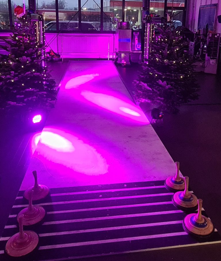 Lila beleuchtetem Laufsteg mit Holzständern und Weihnachtsbäumen im Hintergrund.