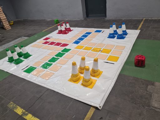 Bodenbrettspiel mit bunten Pylonen in rot, blau, gelb und orange in einem Innenraum.