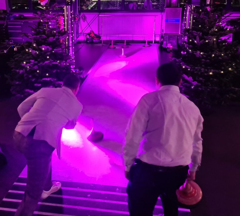 Zwei Personen spielen Bowling auf einer neonbeleuchteten Bahn zwischen Weihnachtsbäumen.