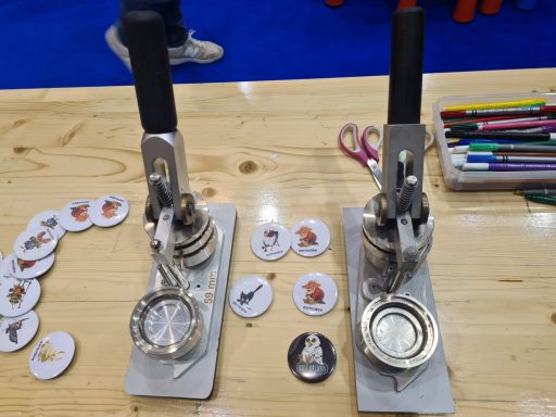 Zwei Button-Maker-Maschinen auf einem Tisch, umgeben von Bastelmaterialien und Buttons.