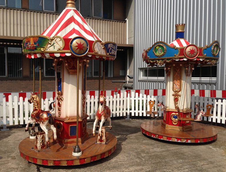 Merlinskarussell und Kettenkarussell - Kettenflieger Zwei nostalgische Karussells mit bemalten Pferden vor einem weißen Zaun.