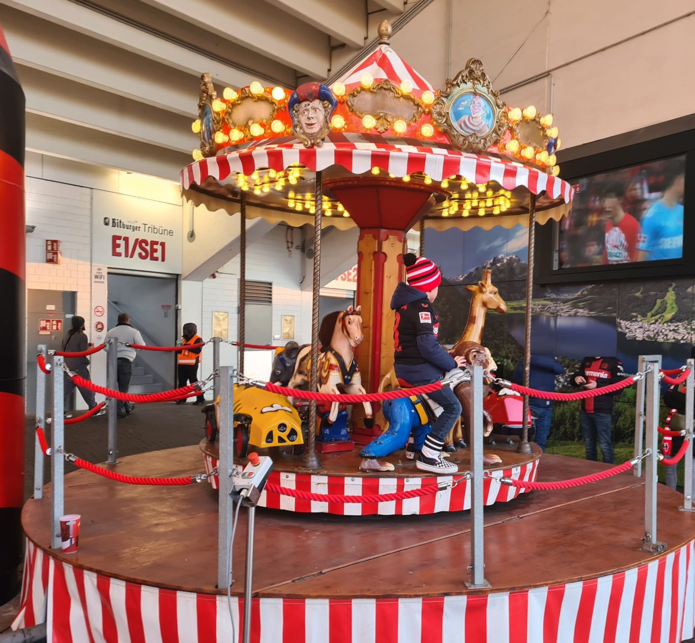 Podiumkarussell Karussell mit roten und weißen Streifen, Kinder fahren auf bunten Tieren.