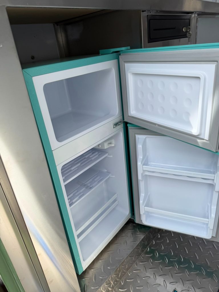 Türkiser Kühlschrank mit offenem Tür, Innenräume leer und unbenutzt.