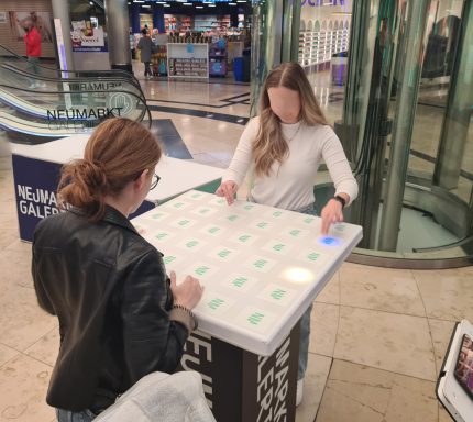 Zwei Frauen stehen an einem interaktiven Tisch mit grünen Symbolen.