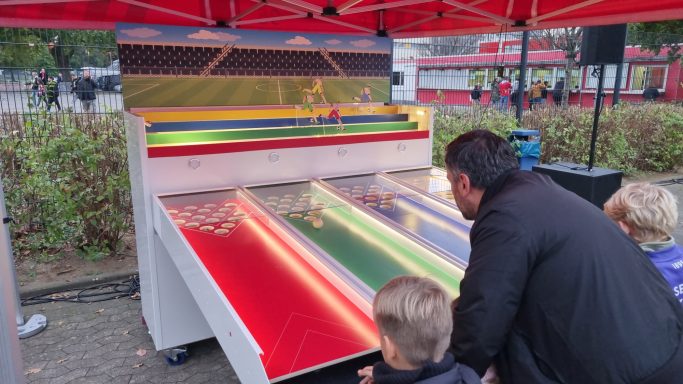 Zwei Kinder und ein Erwachsener spielen an einem bunten Wettlaufspiel im Freien.