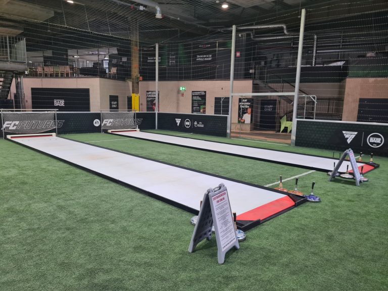 Zwei lange, weiße Trainingsflächen in einer Indoor-Sportanlage mit Rasen.