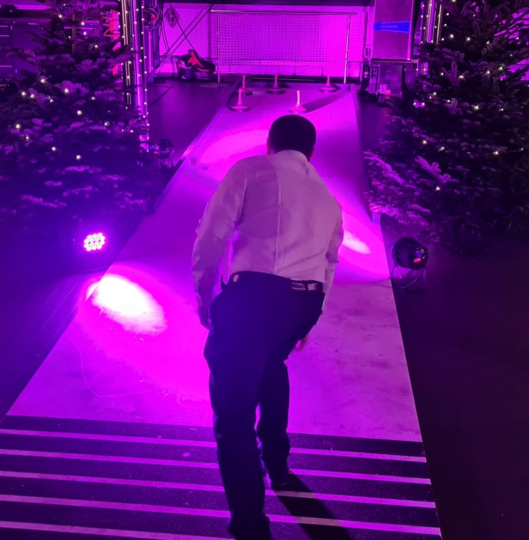 Mann in weißem Hemd geht eine beleuchtete Plattform in lila Beleuchtung entlang.