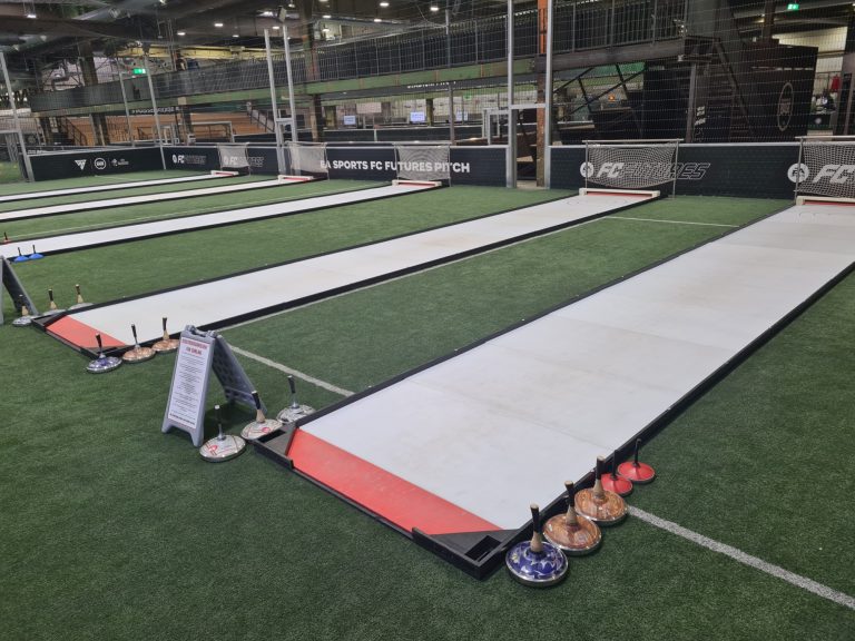 Zwei lange Bahnen auf einem Sportfeld, bereit für Curling oder ähnlichen Sport.