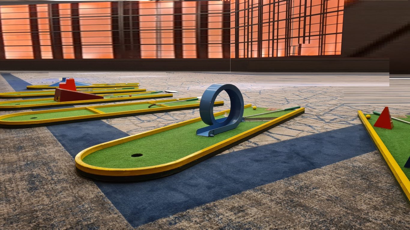 Mini Golf Miniaturgolfbahn mit bunten Hindernissen und einer runden Durchfahrt auf grünem Rasen.