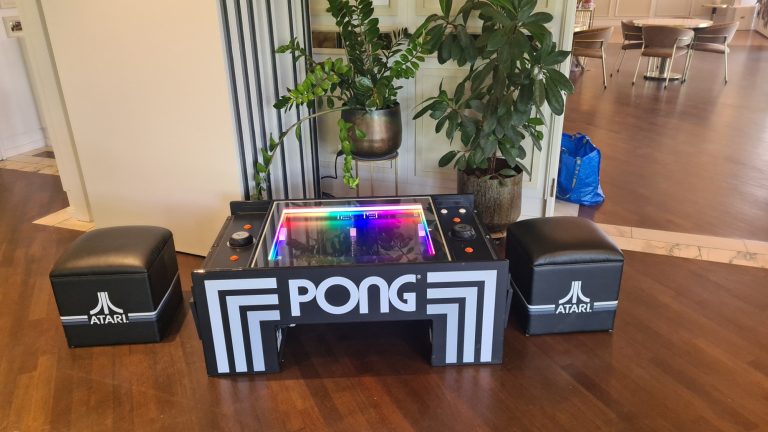 Spieltisch für Pong mit bunten Lichtern und zwei Sitzhockern in einem modernen Raum.