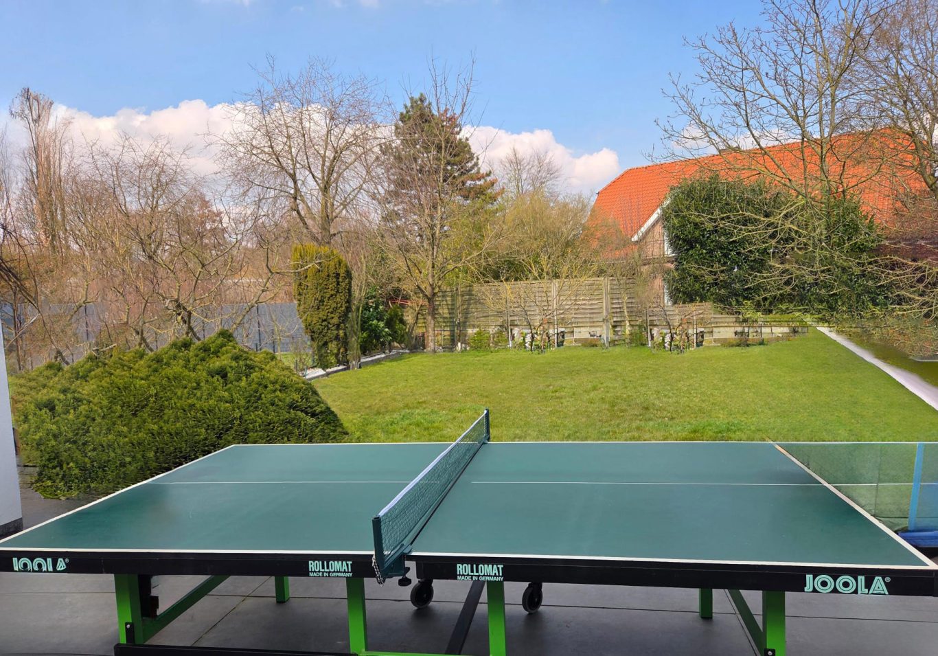 Tischtennisplatte Tischtennisplatte auf einer Terrasse mit Blick auf einen Garten und blauen Himmel.