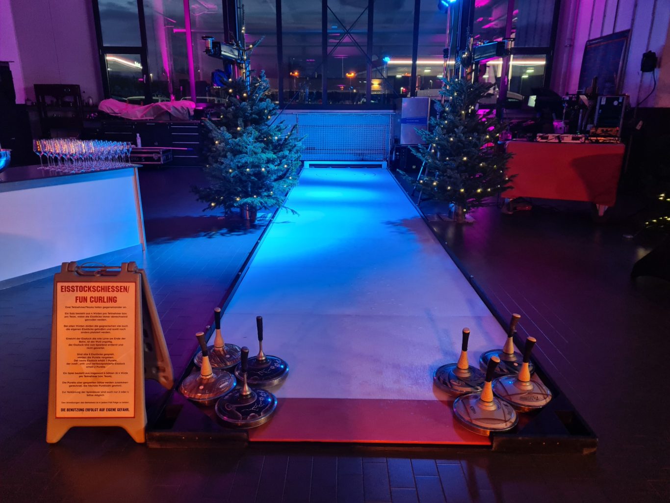 Eisstockschiessen - Fun Curling Blick auf eine festlich beleuchtete Bahn mit Weihnachtsbäumen und Dekoration.
